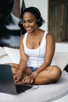 Smiling woman in headphones using a laptop at home, enjoying remote work.