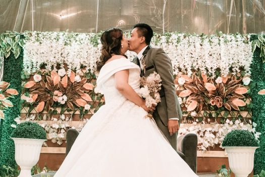 Bride and groom kissing in front of a floral backdrop during a wedding ceremony.