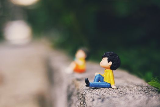Colorful small couple figurines placed on concrete surface on street with lush green trees on blurred background on summer day