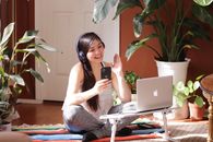 Woman in White Tank Top and Gray Pants Sitting on Floor Using Silver Macbook