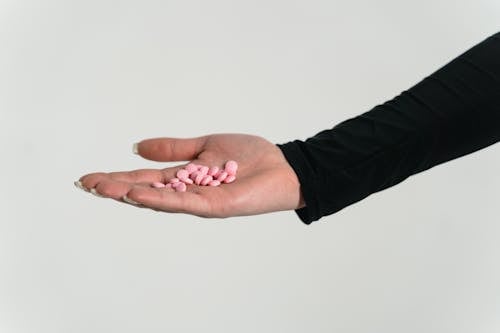 Free Close-Up Shot of a Person Holding Pink Pills on White Background Stock Photo