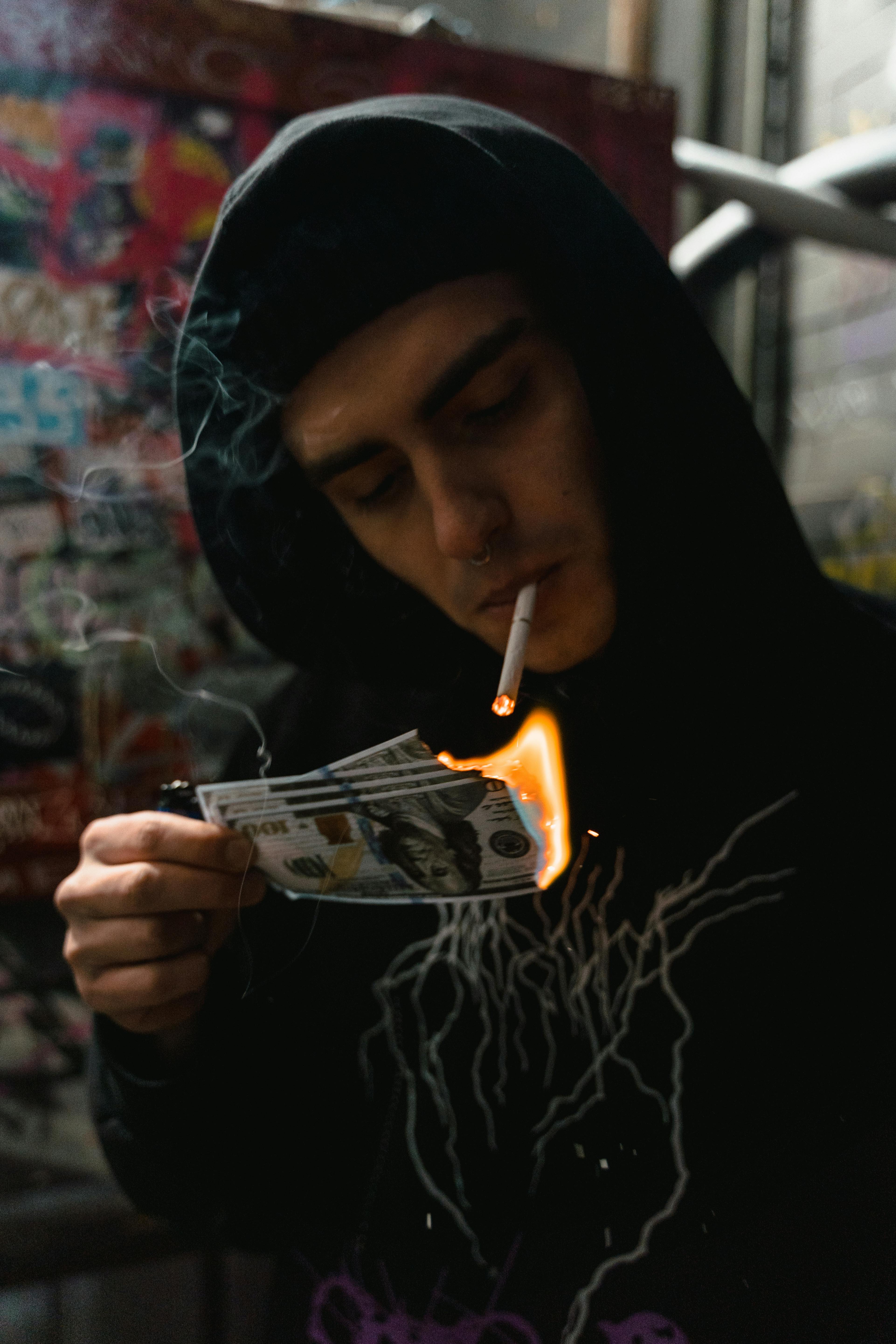a man in black hoodie smoking cigarette while burning money