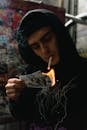 A Man in Black Hoodie Smoking Cigarette while Burning Money