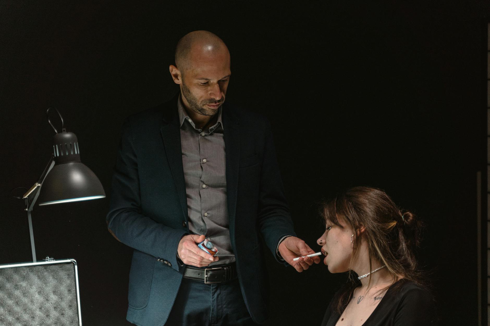 Intense interrogation scene featuring a man and woman under a dim light.