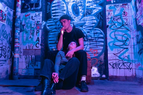 A Man in Black Shirt Smoking Cigarette while Sitting Near the Woman Looking Up on Him