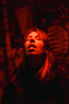 Intense portrait of a woman in a dimly lit room with red lighting, evoking strong emotions.