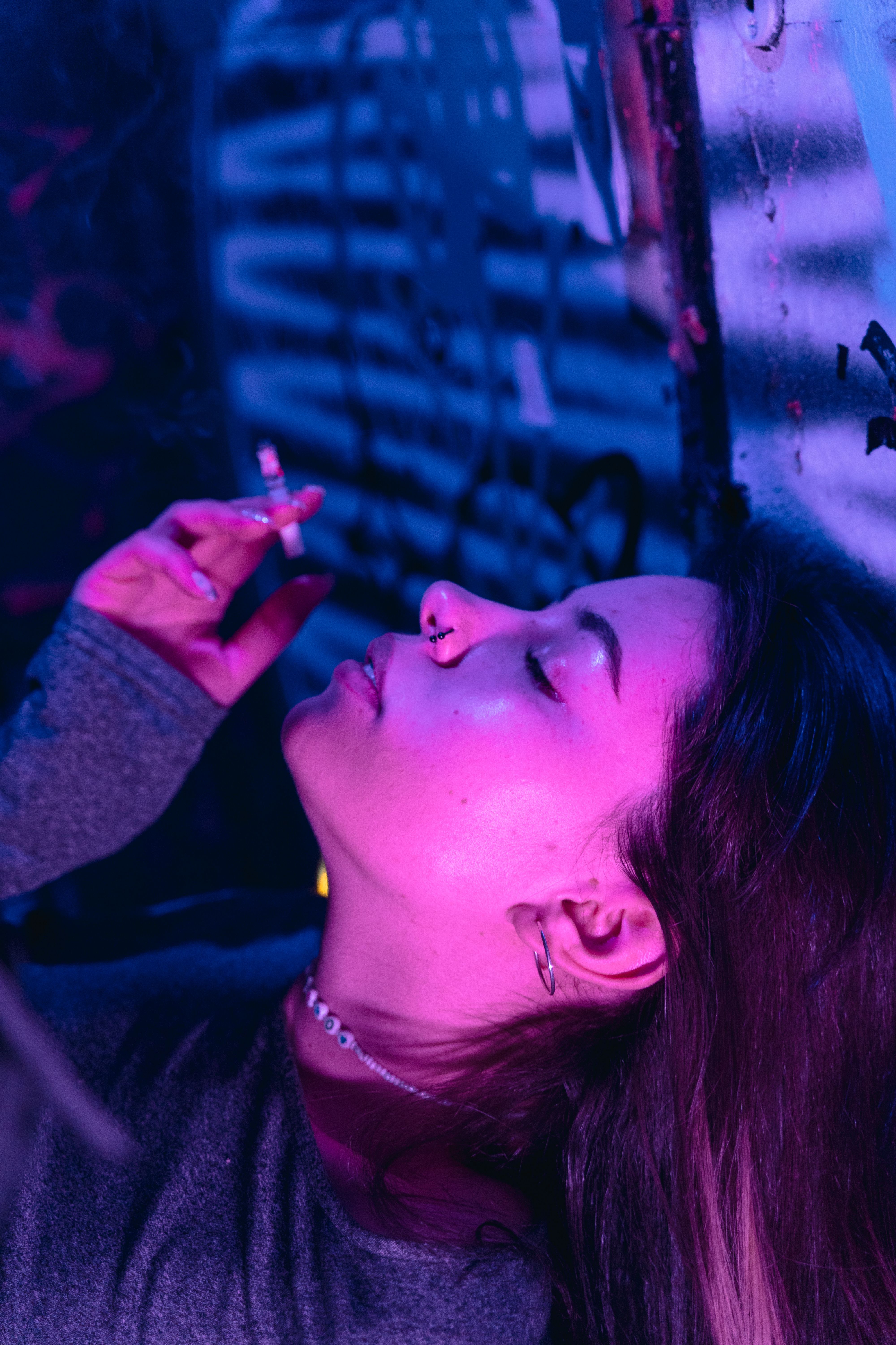 A young woman smoking indoors with head back, in dim neon lighting.