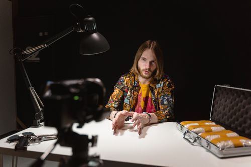 Free A dramatic scene depicting a man in an interrogation room discussing on camera, with a suitcase and gun visible. Stock Photo
