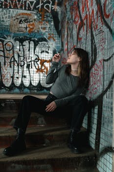A woman sitting on graffiti-covered stairs, smoking in an urban setting.