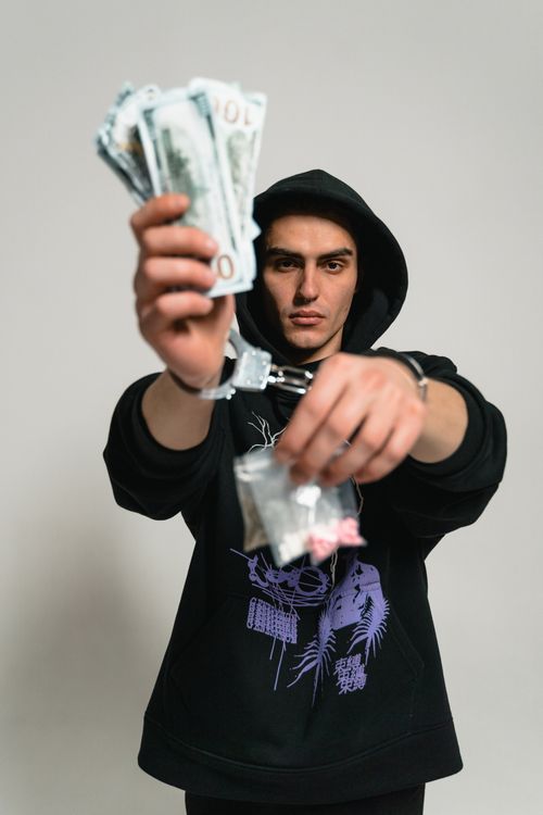 Free A hooded figure holds cash and handcuffs, symbolizing crime and investigation. Stock Photo