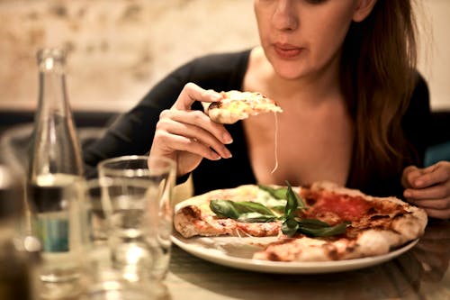 Free Woman Holds Sliced Pizza Seats by Table With Glass Stock Photo