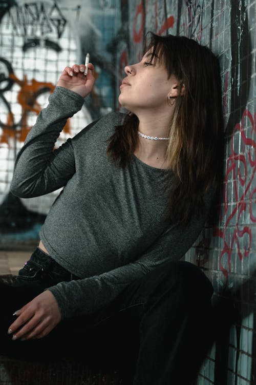 Woman in Gray Long Sleeve Shirt and Black Pants Smoking Cigarette