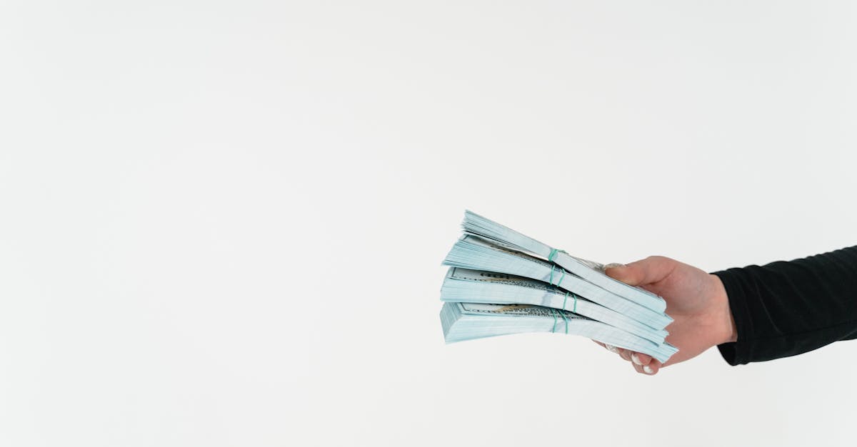 Photo by MART PRODUCTION Close-up of a hand holding bundles of American dollar bills against a white background.