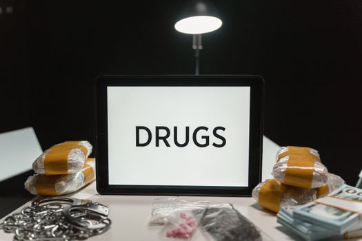Conceptual image of drugs, money, and handcuffs on a table under harsh light, depicting crime themes.