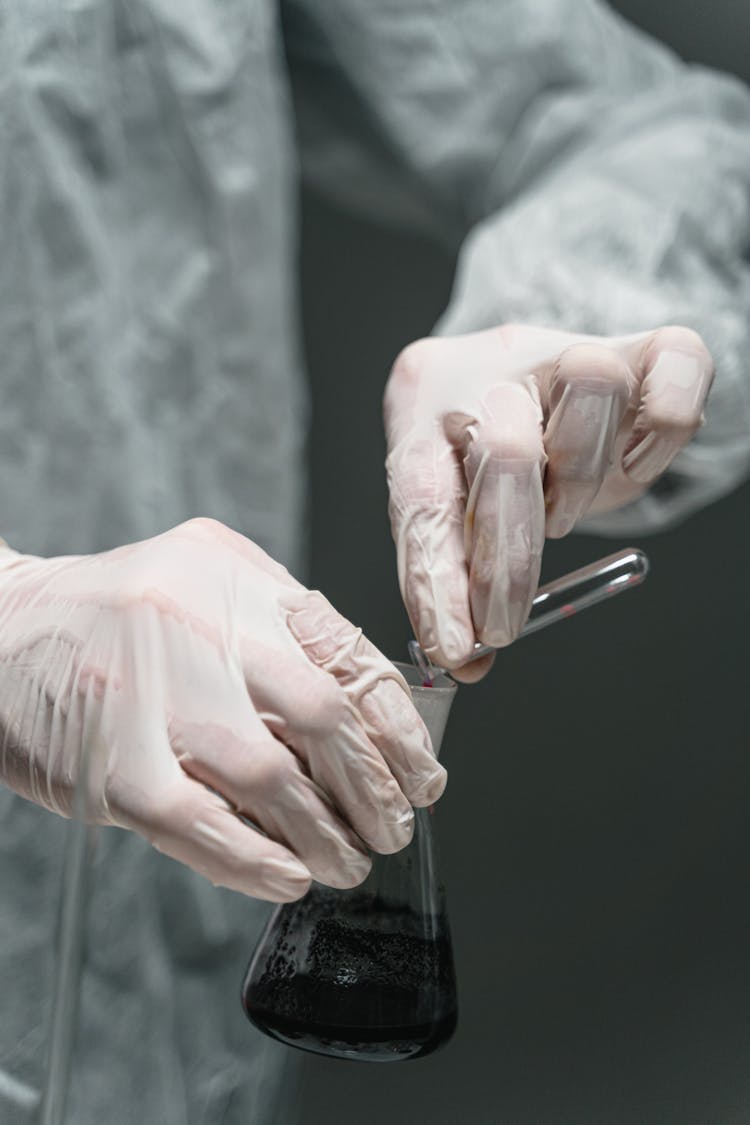 Person In Personal Protective Equipment Holding A Glass Flask Doing Experiment In A Laboratory