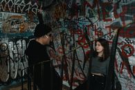 Woman in Black Jacket Standing Beside Graffiti Wall