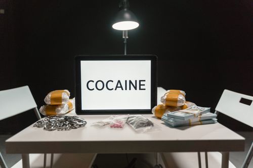 Free Cocaine word on tablet with bags of drugs in a dimly lit room. Stock Photo