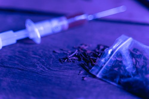 Free Close-up of a syringe and a bag of dried substance with blue lighting. Stock Photo