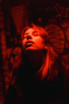 Moody portrait of a woman under red lighting against graffiti backdrop.