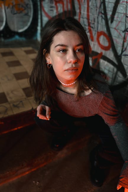 Portrait of a young woman in a graffiti-covered urban setting, gazing thoughtfully.