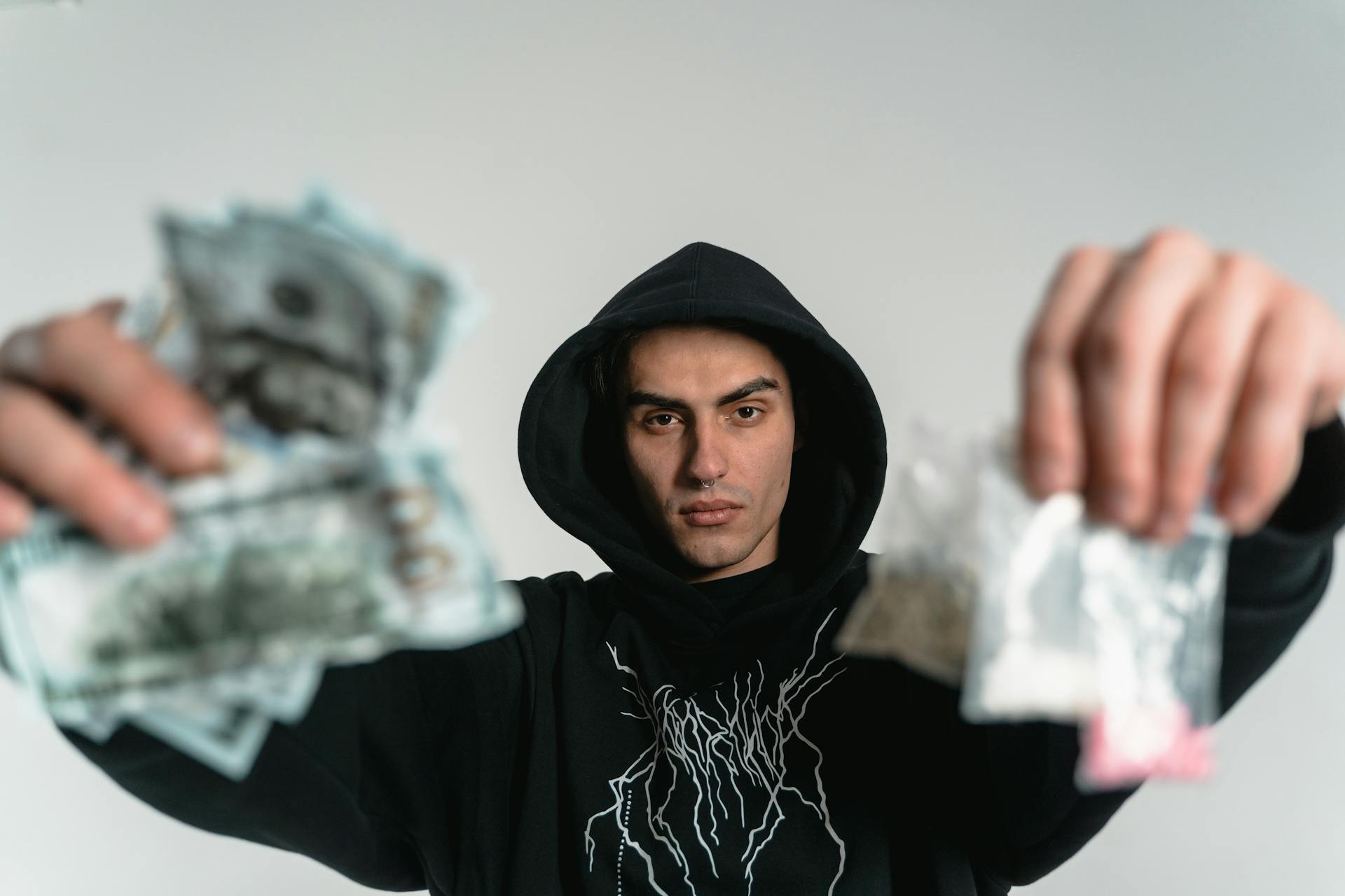 Close-up of a young man in a hoodie holding money and unidentified items, depicting urban life.