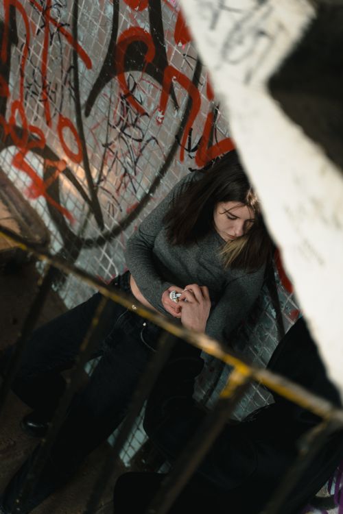 Free Woman with long sleeves sitting near a graffiti-covered wall, urban environment. Stock Photo