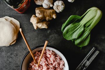 Ground pork in a bowl with dumpling wrappers, ginger, garlic and bok choy
