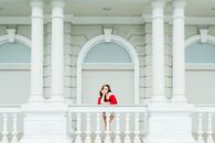 Woman in Red Long Sleeve Shirt Standing Near White Concrete Building