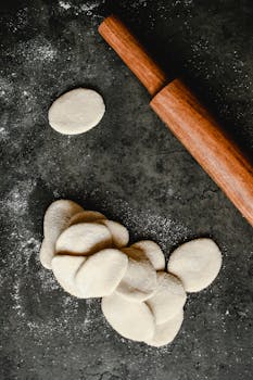 Overhead shot of raw dough circles and a wooden rolling pin on a floured surface.