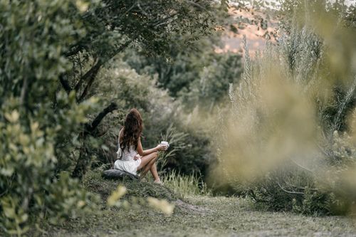 Free Woman in a white dress enjoying coffee in a lush green forest setting. Stock Photo