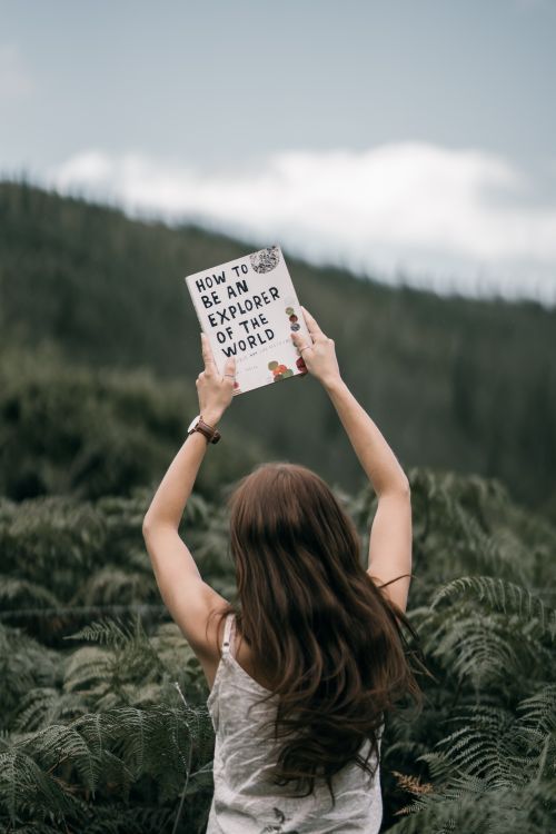 Free Woman holding a book in a verdant forest, symbolizing adventure and exploration. Stock Photo