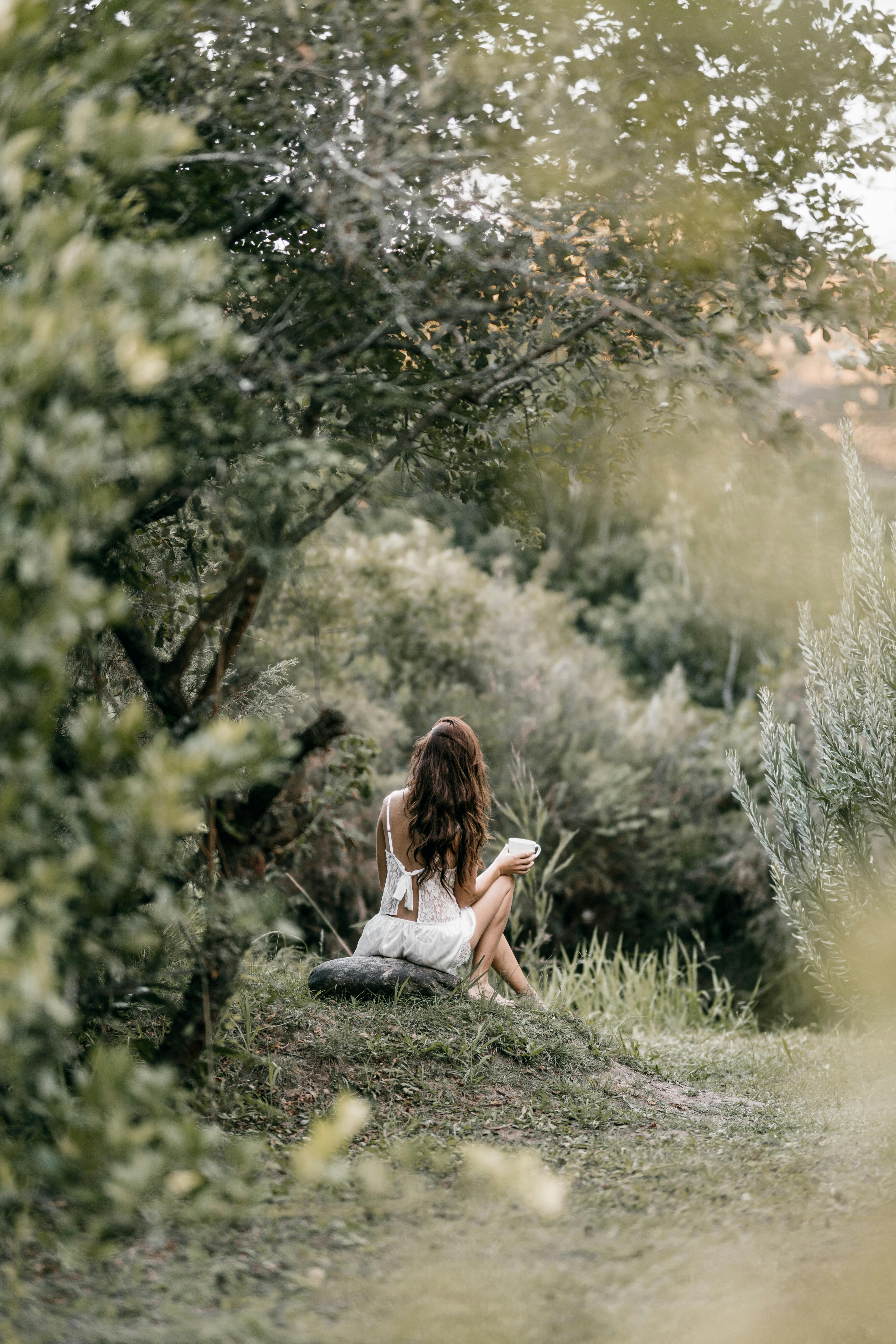 A woman sitting on grass, embracing nature's tranquility in a lush forest setting.