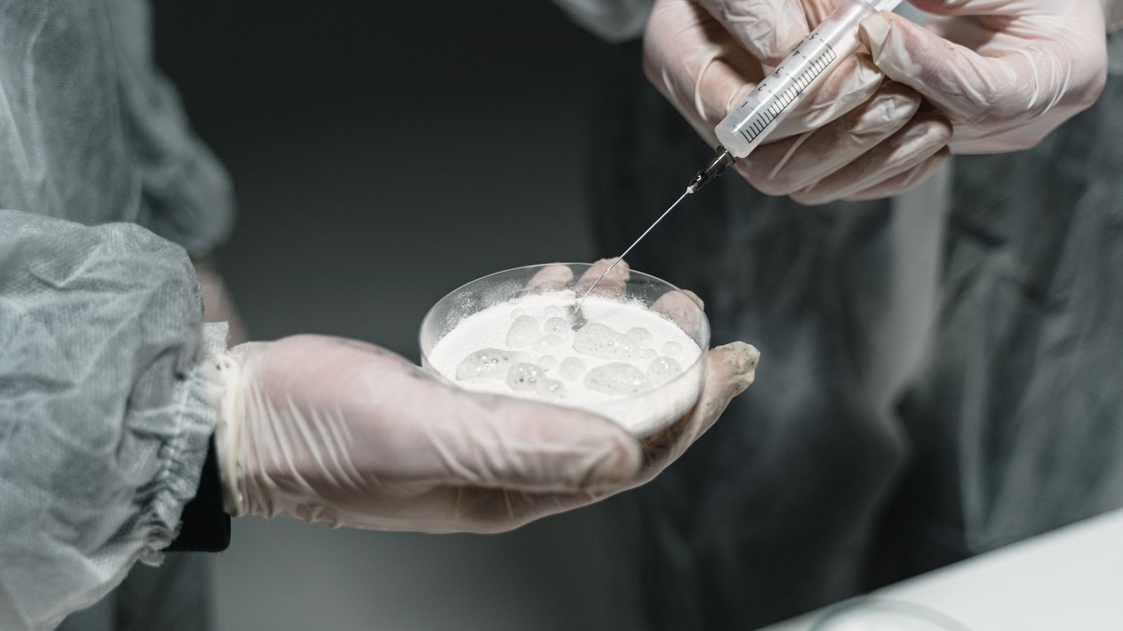 Researchers conducting a scientific experiment with a syringe and petri dish in a lab setting.