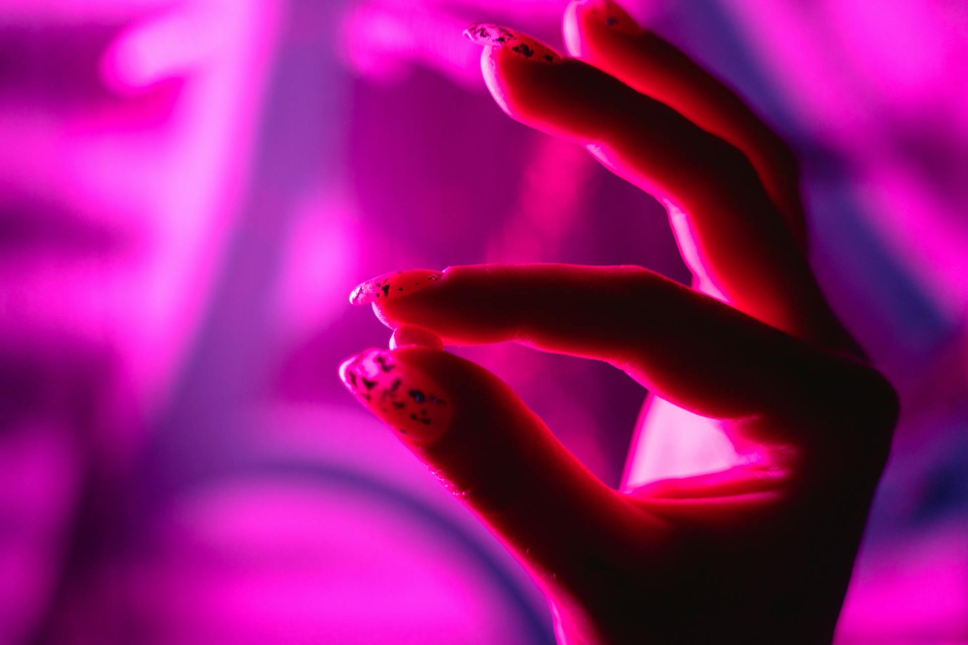 A striking close-up of a hand with nail art illuminated by vibrant pink neon light, showcasing modern style.