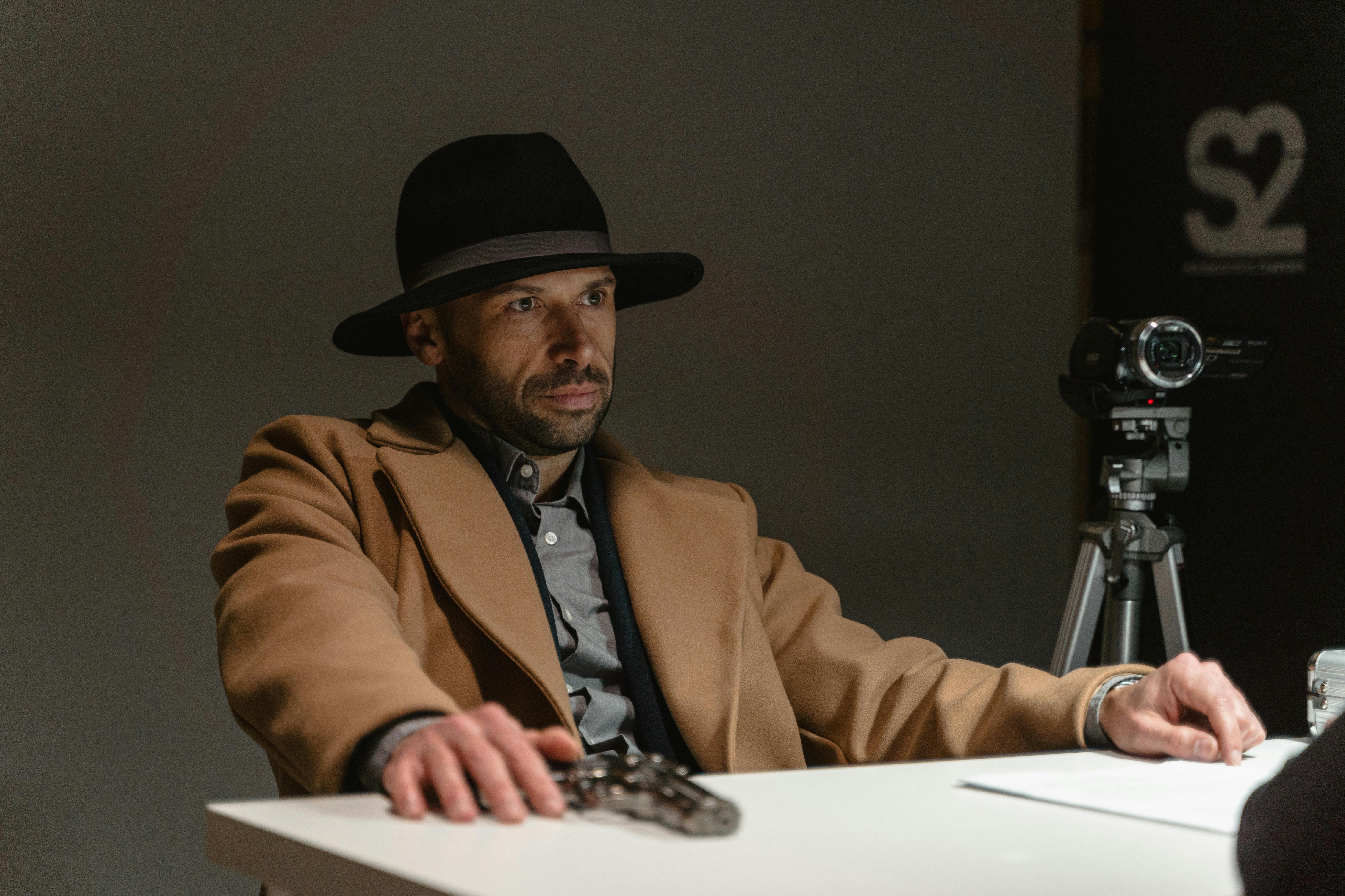 man in brown coat and black hat sitting by the table