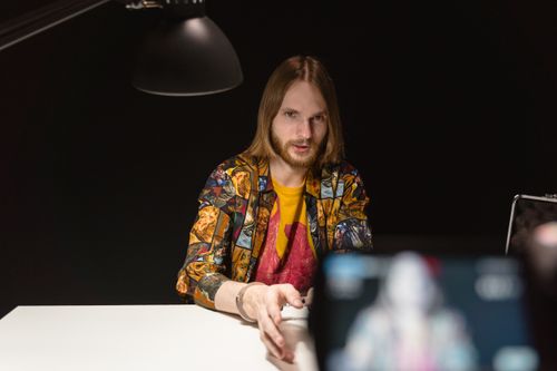 Free Caucasian man sitting under a lamp in a dark interrogation room setting. Stock Photo