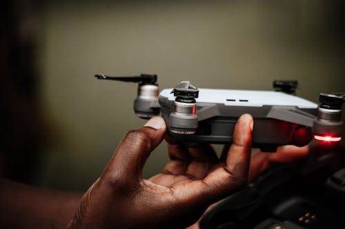 Crop unrecognizable ethnic person turning on unmanned aerial vehicle with shiny light and propellers