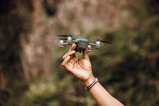 Crop anonymous person demonstrating unmanned aerial vehicle in raised hand in daylight on blurred background