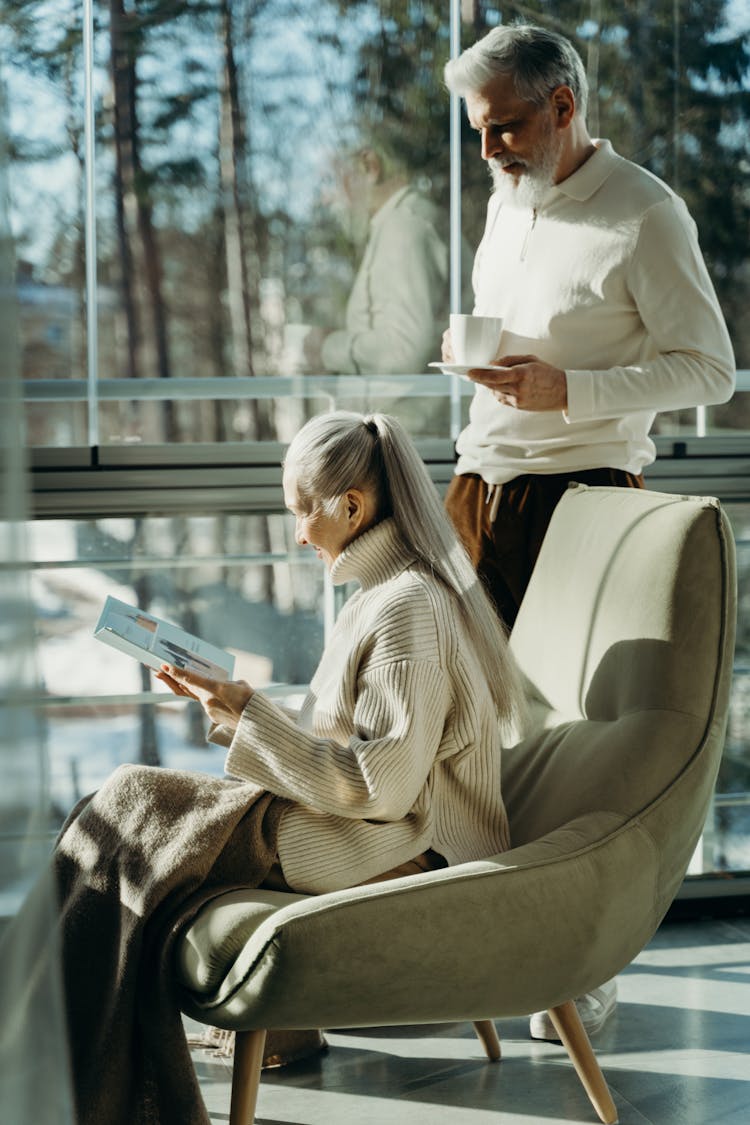 Elderly Man Standing Beside Elderly Woman Sitting On Chair