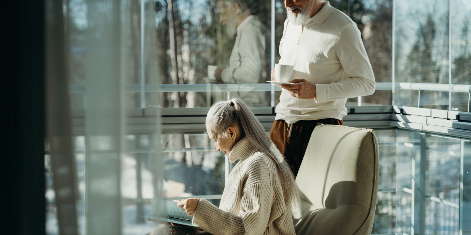 Elderly couple enjoying a serene moment indoors with natural lighting, sipping coffee.