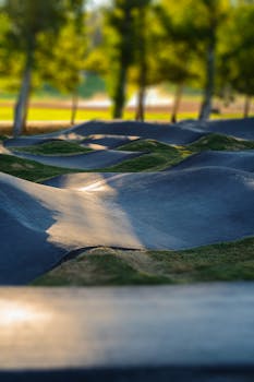 A scenic pump track with smooth curves and lush greenery in a sunlit park.