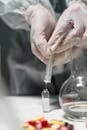 Person Holding a Syringe Putting Liquid Inside a Glass Vial