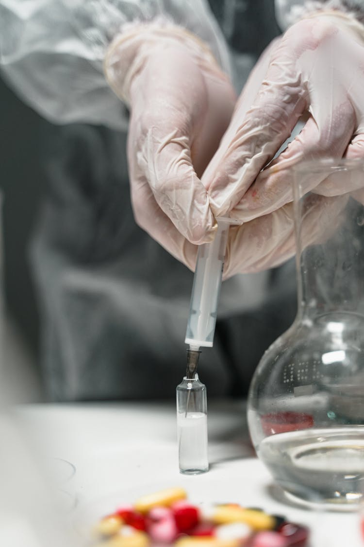 Person Holding A Syringe Putting Liquid Inside A Glass Vial