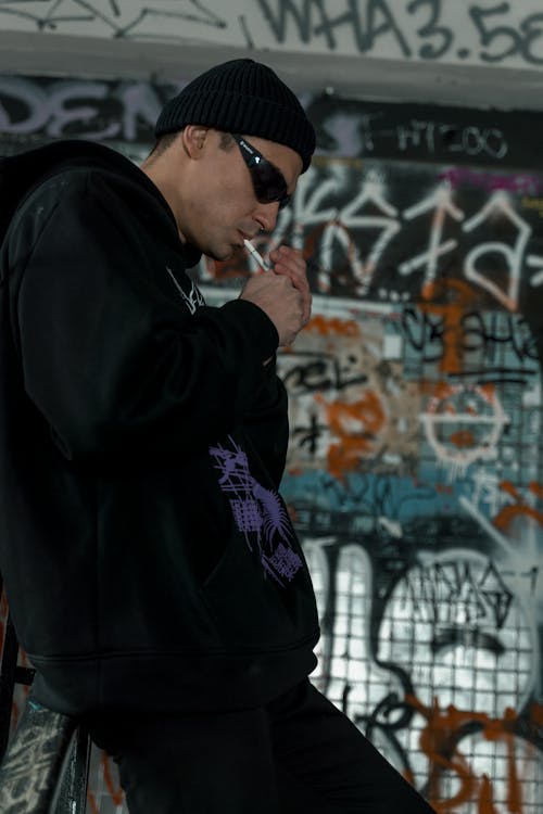 A Man Wearing a Beanie and Shades Lighting a Cigarette