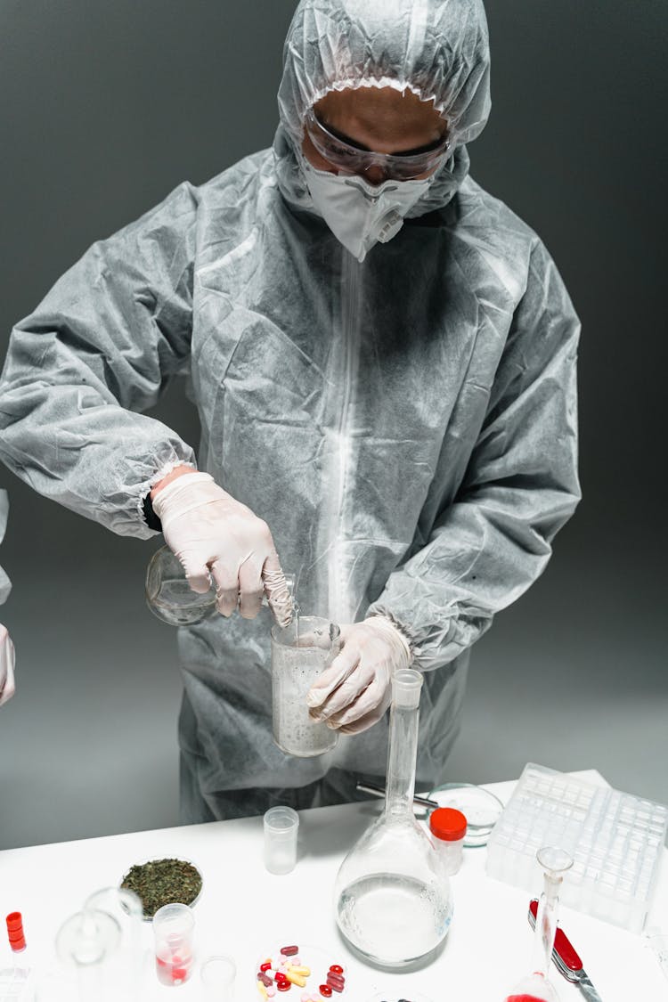 Person Standing In Personal Protective Equipment Holding A Glass Test Tubes Doing Experiment In A Laboratory