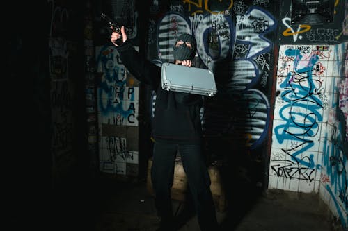 Free Anonymous Person Wearing Mask while Holding Gun and Gray Briefcase Stock Photo