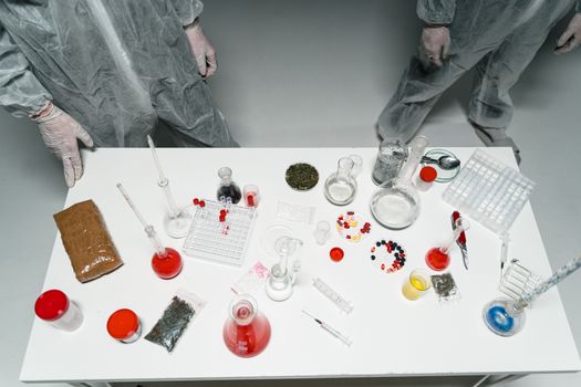 Top view of a laboratory setup with various scientific tools and substances, featuring researchers in lab coats.