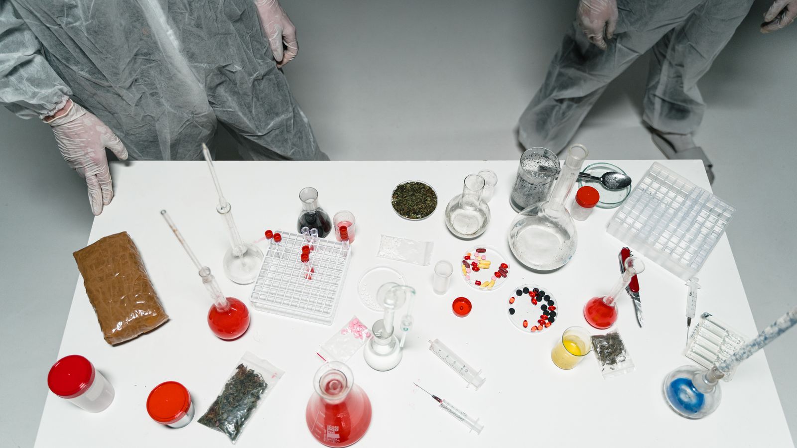 Top view of a laboratory setup with various scientific tools and substances, featuring researchers in lab coats.