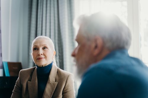 Free Elderly man and woman engaged in a warm conversation, sunlight streaming through the window. Stock Photo