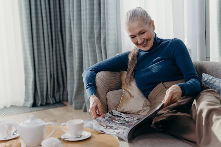 An Elderly Woman Reading A Magazine While Smiling